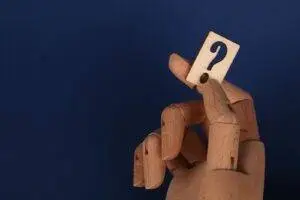 Wooden mannequin hand holding a block with a question mark against a blue background.