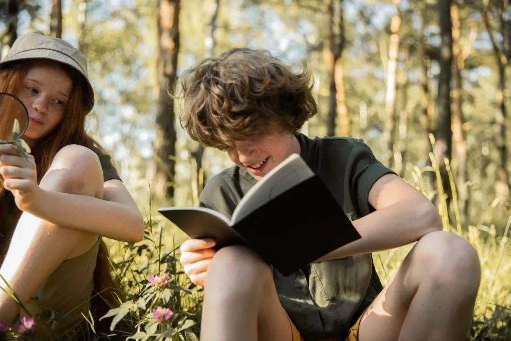 Two teenagers studying in a sunny forest, engaging with nature through reading and exploration.