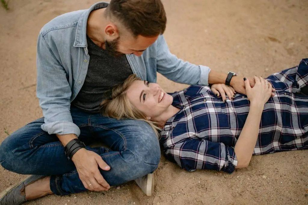 A happy expecting couple lying on sand, showcasing love and anticipation.