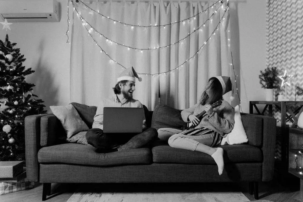 A couple enjoys a cozy Christmas evening with music and laughter in their decorated living room.