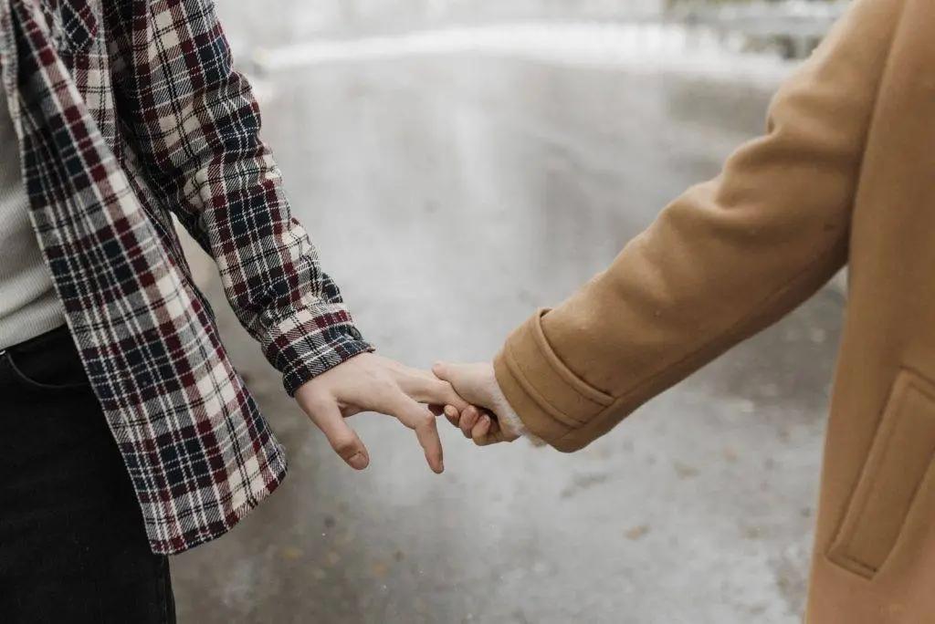 A close-up scene of a couple gently holding hands in an outdoor setting.
