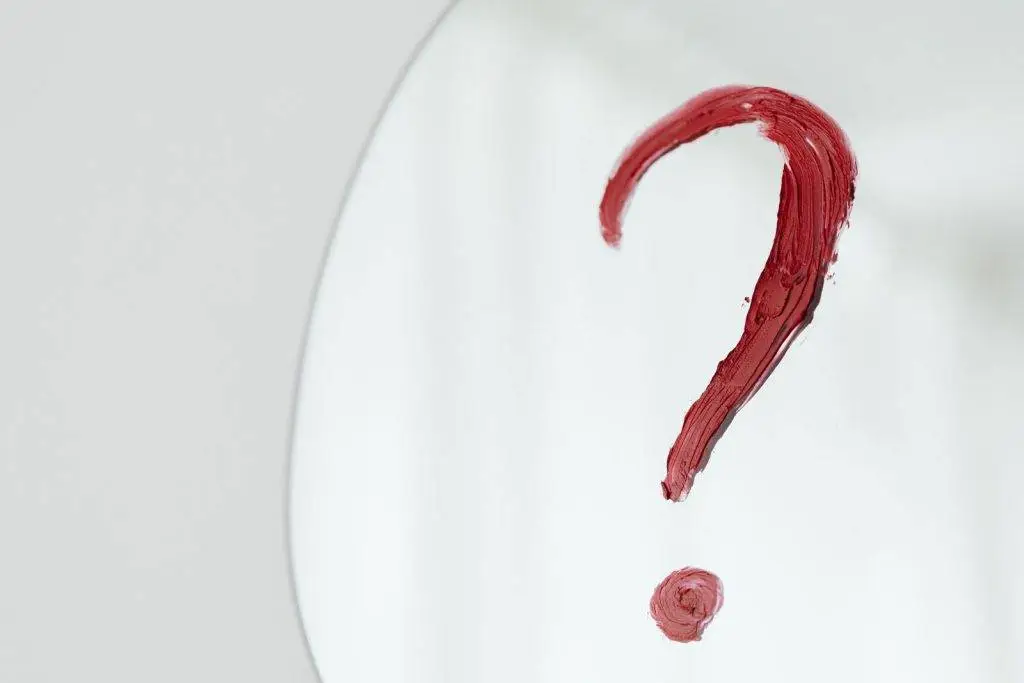 Close-up of a red question mark painted on a mirror with a white background.