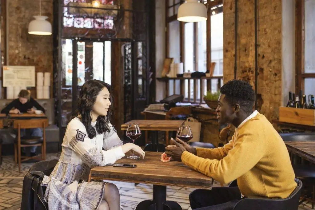 An Asian woman and Black man enjoy a romantic date with wine in a stylish caf&eacute;.