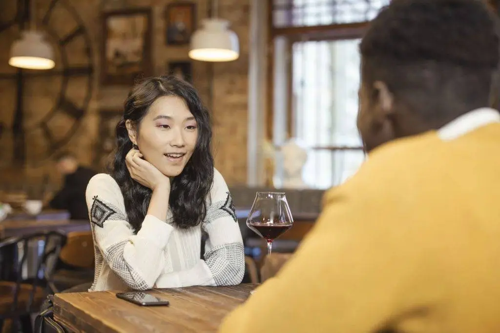 Two adults enjoying a conversation over wine in a warm, cozy caf&eacute; atmosphere.