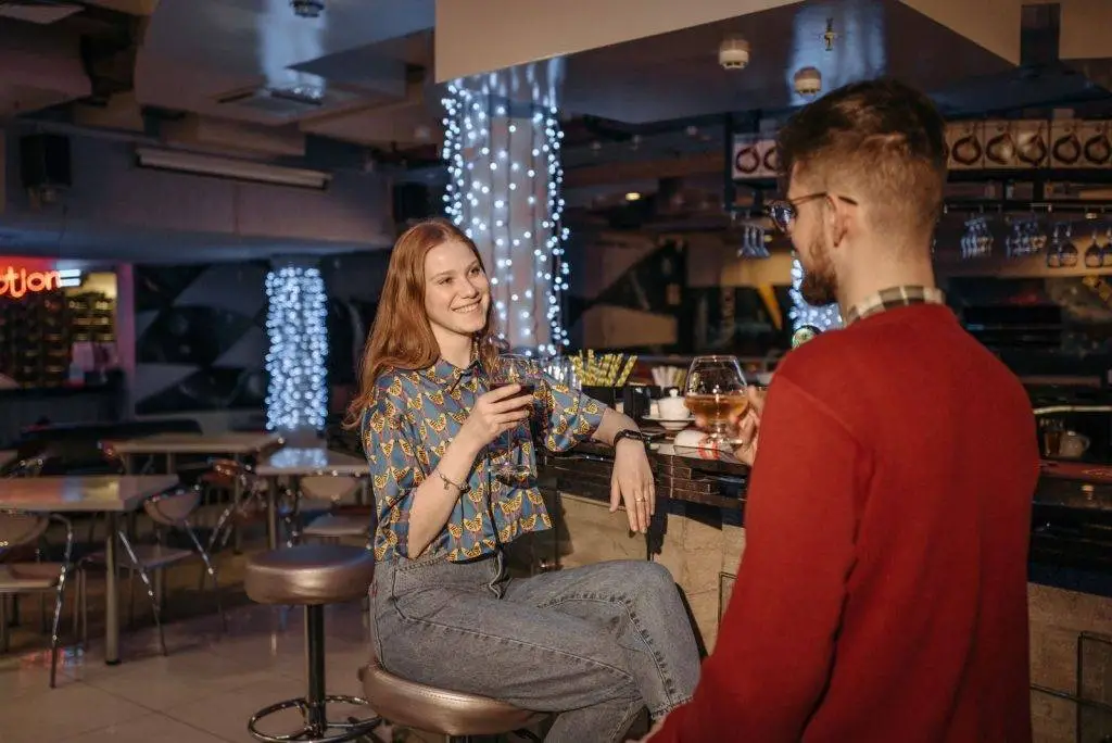 Two adults enjoying drinks at a lively bar setting, exchanging smiles and conversation.